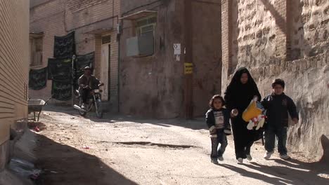 A-woman-wearing-a-chador-walks-with-two-children-down-an-ancient-alley-in-Iran