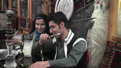 A-woman-wearing-a-headscarf-and-a-man-smoke-a-hookah-pipe-in-an-outdoor-cafe-in-Iran-