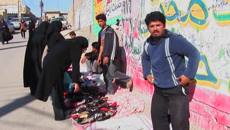 A-women-wearing-chadors-buy-from-vendors-near-a-wall-covered-in-graffiti-in-an-urban-area