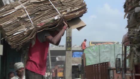 A-worker-carries-a-pile-of-cardboard-on-his-back-and-loads-it-onto-a-truck-along-with-many-other-piles