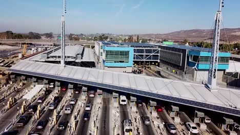 Steigende-Antenne-über-Dem-Grenzübergang-San-Ysidro-Tijuana-Us-Mexiko-Mit-Autos,-Die-Kilometerweit-Aufgereiht-Sind
