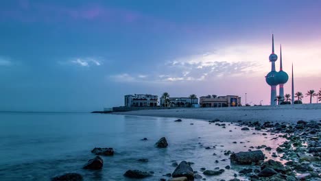 Ein-Zeitraffer-Eines-Sonnenaufgangs-über-Einem-Strand-In-Kuwait-Mit-Dem-Wahrzeichen-Der-Kuwait-Türme-Im-Hintergrund