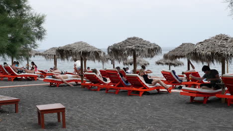 Grecia-Santorini-Perissa-Turistas-Descansando-En-La-Playa-De-Arena-Negra