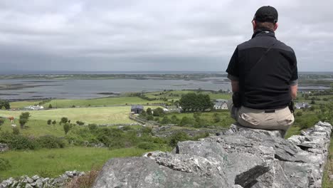 Ireland-County-Clare-Man-On-Wall-Looks-At-Landscape-