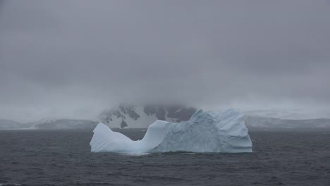 Antarctica-Iceberg-Floats-By-Fog-Covered-Coastline