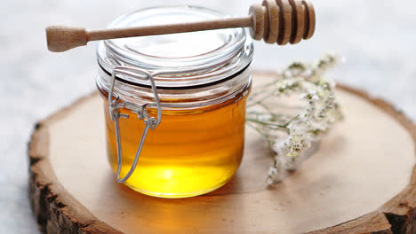 Glass-jar-full-of-fresh-honey-placed-on-slice-of-wood