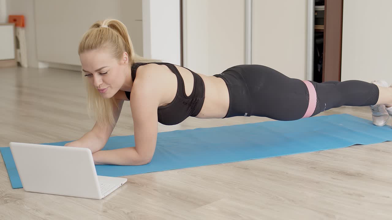 1280px x 720px - Premium stock video - Blond sexy girl doing her gym workout at home while  watching online video lessons on laptop