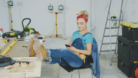 Woman-resting-with-smartphone-at-carpenter-workbench