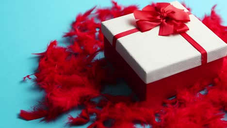 Box-with-a-gift--tied-with-a-ribbon-placed-on-red-feathers