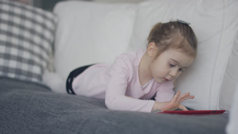 Chilling-little-girl-surfing-tablet-on-couch