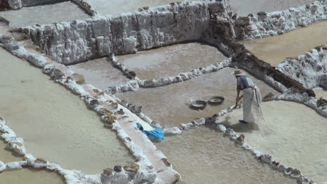 A-woman-works-to-pile-up-salt-in-a-salt-pan-in-the-Andes