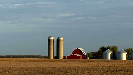 Zooms-out-from-a-red-barn-and-silos-to-a-country-road.