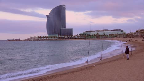 A-large-sailboat-shaped-hotel-stands-on-the-shore-with-fishermen-foreground-Barcelona-Spain