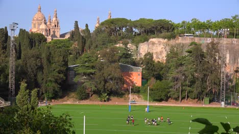 A-football-team-conducts-a-practice-on-a-field-with-Barcelona-National-palace-background