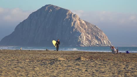 A-surfer-crosses-in-front-of-the-beautiful-Morro-Bay-rock-along-California's-central-coast