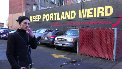 Un-Hombre-Se-Para-Frente-A-Un-Letrero-En-Un-Edificio-Instando-A-Los-Visitantes-A-Mantener-A-Portland-Extraño