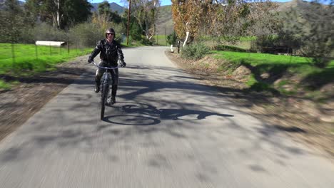 A-man-in-leather-jacket-drives-a-motorized-bicycle-along-a-country-road