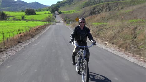 Un-Hombre-Con-Chaqueta-De-Cuero-Conduce-Una-Bicicleta-Motorizada-A-Lo-Largo-De-Una-Carretera-2