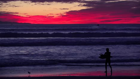 A-surfer-or-wakeboarder-emerges-from-the-waves-at-sunset-along-a-California-beach