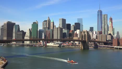 Nice-establishing-shot-of-New-York-City-financial-district-with-Brooklyn-Bridge-foreground-and-boats-passing-under-1