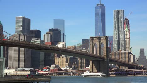Nice-establishing-shot-of-New-York-City-financial-district-with-Brooklyn-Bridge-foreground-and-boats-passing-under-2