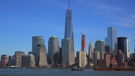 Ein-Schlepper-Zieht-Einen-Lastkahn-Auf-Dem-Hudson-River-In-New-York-City-Mit-Dem-Freiheitsturm-Hintergrund