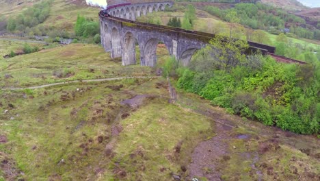 Eine-Erstaunliche-Luftaufnahme-über-Das-Glenfinnian-Viaduct-In-Schottland-Mit-Vorbeifahrender-Dampfbahn