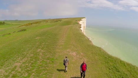 Toma-Aérea-De-Gente-Caminando-Por-Los-Acantilados-Blancos-De-Dover-En-Beachy-Head-Inglaterra