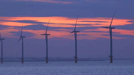 Windmills-generate-electricity-along-a-coastline-at-sunset
