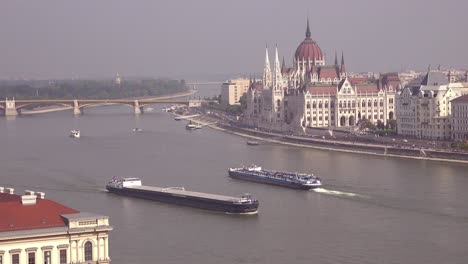 Budapest-Hungría-Y-El-Parlamento-Mientras-Las-Barcazas-Se-Mueven-A-Lo-Largo-Del-Río-Danubio