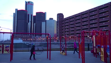 Der-GM-Turm-In-Der-Abenddämmerung-Entlang-Des-Detroit-River-In-Detroit-Michigan-Mit-Spielenden-Kindern-Im-Vordergrund-1