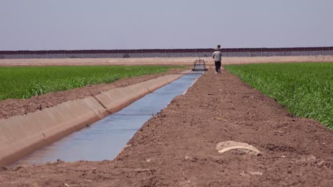 Un-Agricultor-Camina-A-Lo-Largo-De-La-Frontera-Entre-Estados-Unidos-Y-México-Con-El-Muro-Al-Fondo