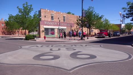 Toma-De-Establecimiento-Del-Centro-De-Winslow,-Arizona-Con-Un-Mural-Que-Representa-Un-Ford-De-Superficie-Plana-Y-El-Letrero-De-La-Ruta-66