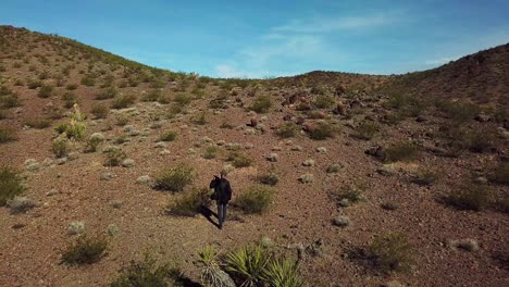 Drone-vista-aérea-of-a-photographer-walking-with-and-tripod-across-a-desert-with-long-shadows