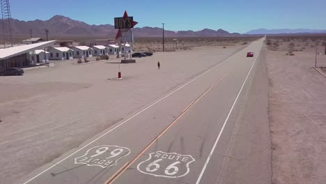 Antena-De-Drone-Sobre-Una-Carretera-Del-Desierto-Solitario-En-Arizona-Con-La-Ruta-66-Pintada-Sobre-El-Pavimento-Y-El-Coche-Pasando-Por-Debajo