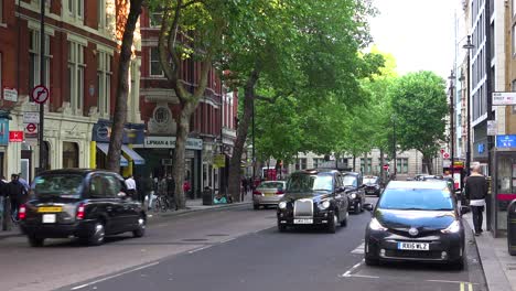 Traditional-London-taxi-cabs-head-down-a-street-in-a-downtown-neighborhood