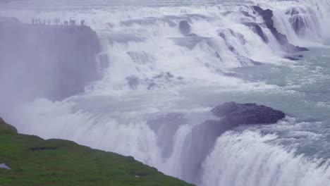Der-Spektakuläre-Und-Massive-Wasserfall-Gullfoss-Fließt-In-Island-Mit-Touristen-Auf-Einer-Klippe-In-Der-Ferne