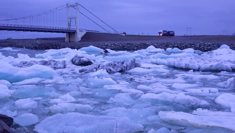 Un-Coche-Y-Un-Camión-Cruzan-Un-Puente-Sobre-Una-Bahía-Glacial-En-El-Ártico-En-La-Laguna-Glaciar-Jokulsarlon-Islandia-Noche