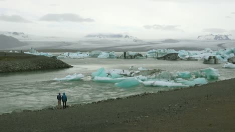 Two-people-stand-along-a-river-in-the-frozen-Arctic-Jokulsarlon-glacier-lagoon-in-Iceland-suggesting-global-warming