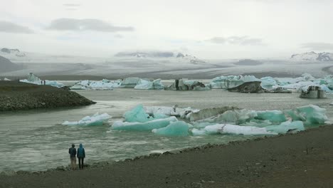 Two-people-stand-along-a-river-in-the-frozen-Arctic-Jokulsarlon-glacier-lagoon-in-Iceland-suggesting-global-warming-1