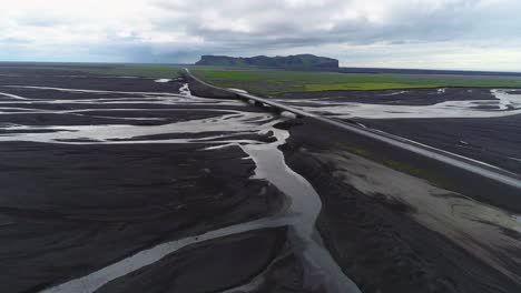 Aerial-along-a-road-and-bridge-over-a-large-dark-volcanic-flood-river-system-in-Iceland