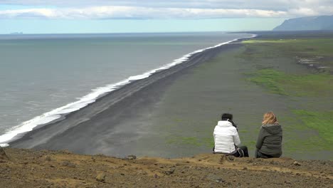 Zwei-Frauen-Sitzen-Auf-Einer-Klippe-Mit-Blick-Auf-Dyrh_____‚laey-Black-Sand-Beach-Island