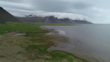 Atemberaubende-Luftaufnahme-Von-Bemerkenswert-Schönen-Fjorden-In-Island-Mit-Wolken-Und-Nebel,-Die-über-Die-Spitze-Rollen