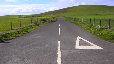 An-empty-road-leads-through-brilliant-green-fields-in-the-Orkney-Islands-of-Scotland