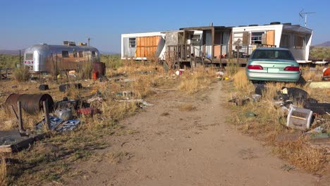 An-abandoned-mobile-home-in-the-desert-is-surrounded-by-old-trucks-and-cars-and-trash-4