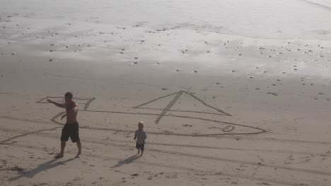 Ein-Vater-Und-Kinder-Zeichnen-Am-Strand-Ein-Segelboot-In-Den-Sand-1