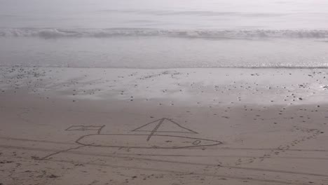 A-sailboat-is-drawn-in-the-sand-on-a-beach