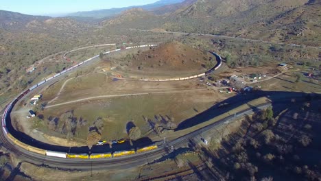 An-vista-aérea-over-a-freight-train-travels-the-remarkable-Tehachapi-Loop-in-California\'s-desert-making-a-full-circle-around-itself