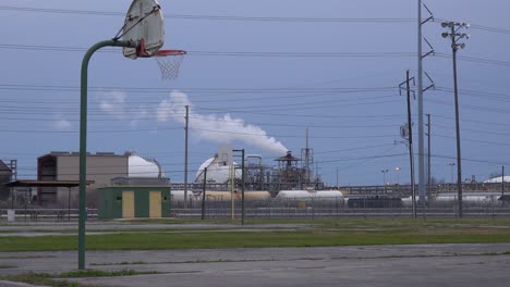 An-empty-basketball-court-stands-in-front-of-a-large-oil-refinery