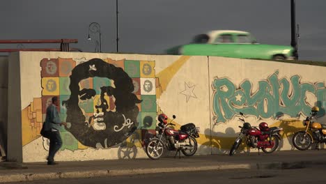 A-car-drives-down-a-road-near-a-building-decorated-with-Che-revolutionary-painting-in-Communist-Cuba